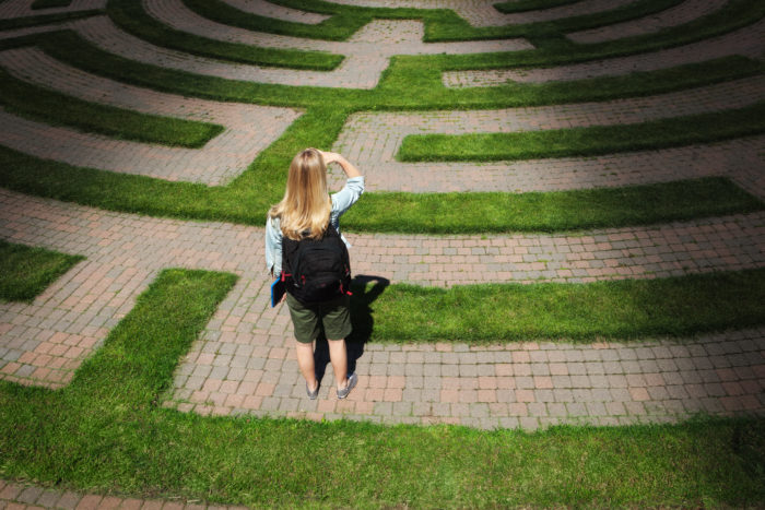 A woman teenager student stands looking through the puzzling maze of schooling and the education system, forecasting the way forward and searching for the path to her goal. Concept of student facing uncertainty to their education, life and future career.